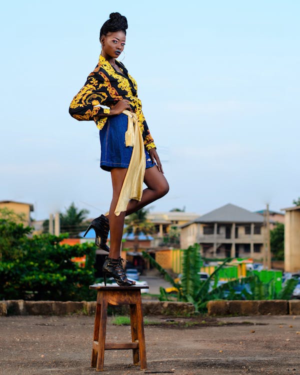 Free Woman in Black and Yellow Top and Blue Skirt Standing on Brown Wooden Stool Stock Photo