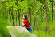 一位穿着红色衬衫的年轻女子微笑着，在郁郁葱葱的绿色森林环绕的木凳上摆姿势