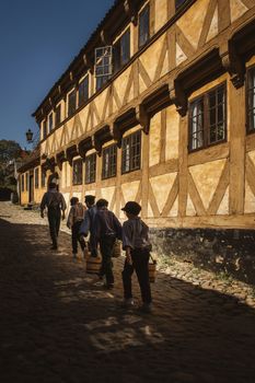 Children dressed in historical attire walk on a cobblestone street in Aarhus, Denmark.