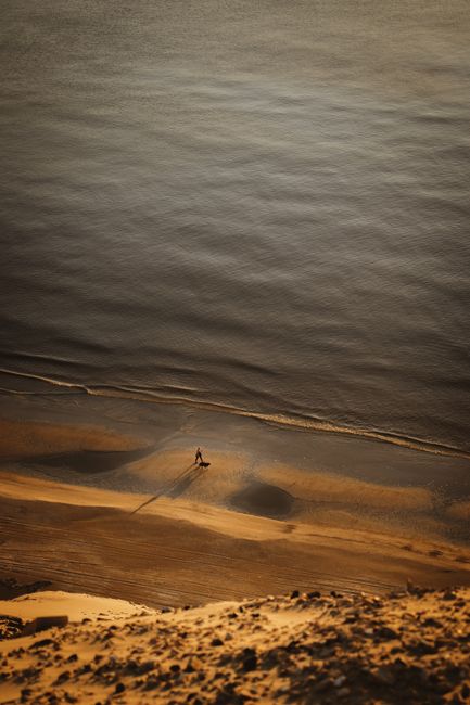 A person walks on Løkken beach, Denmark during sunset, casting a long shadow on the sand.