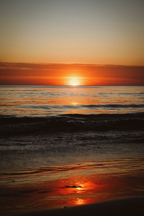 Free Vibrant sunset over Løkken beach with calm ocean waves reflecting warm hues. Stock Photo