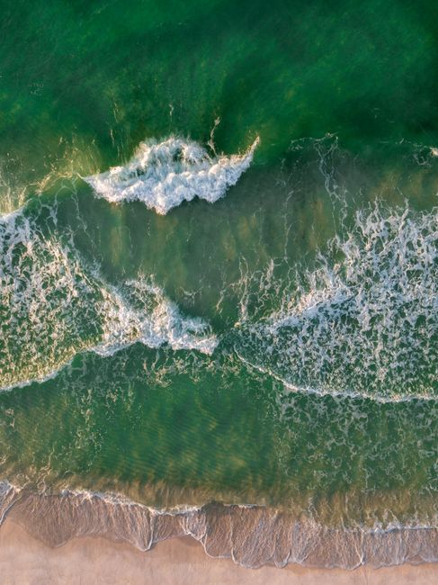 A stunning aerial shot of turquoise ocean waves crashing onto a sandy beach, capturing summer's essence.