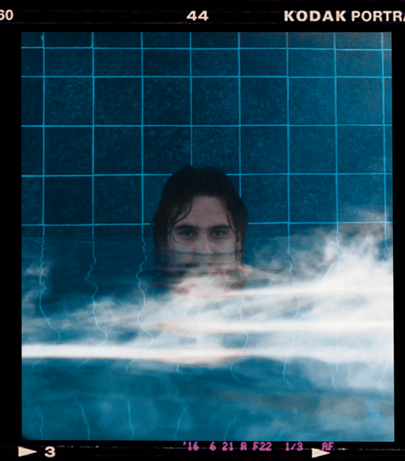 A person partially submerged in a pool captured in a moody, artistic style.