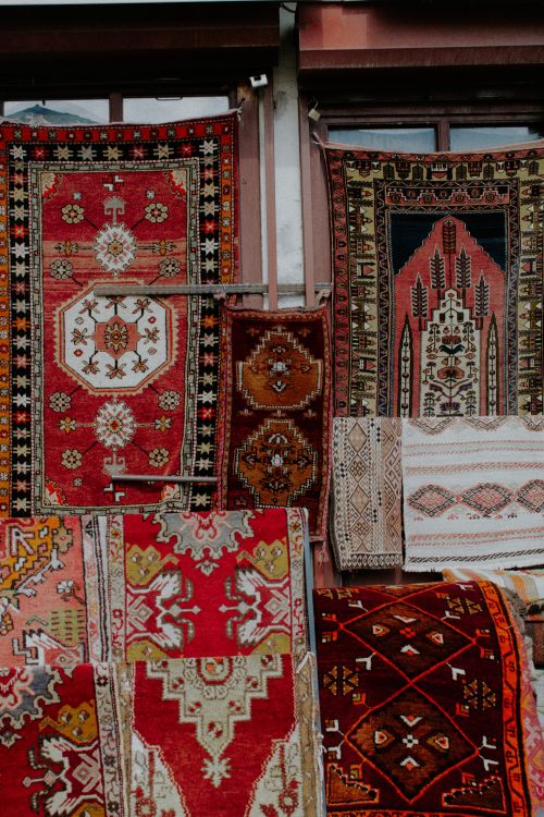 Free A collection of vibrant and ornate rugs, showcasing intricate patterns and textures, hanging in a rustic market setting. Stock Photo