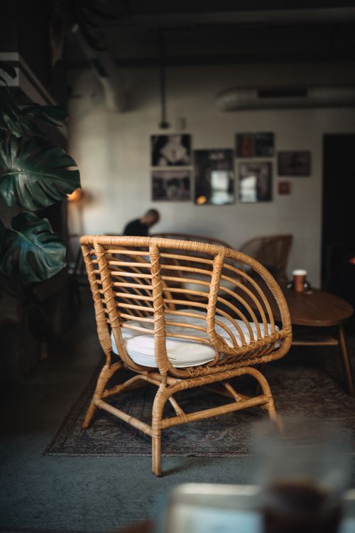 Free Stylish café interior featuring a modern rattan chair and cozy ambiance with houseplants and wall art. Stock Photo