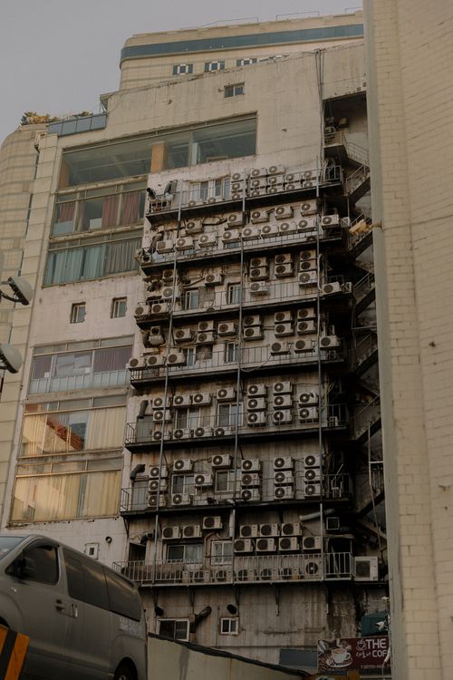 Free A low-angle view of a building's exterior covered with multiple air conditioner units in an urban setting. Stock Photo