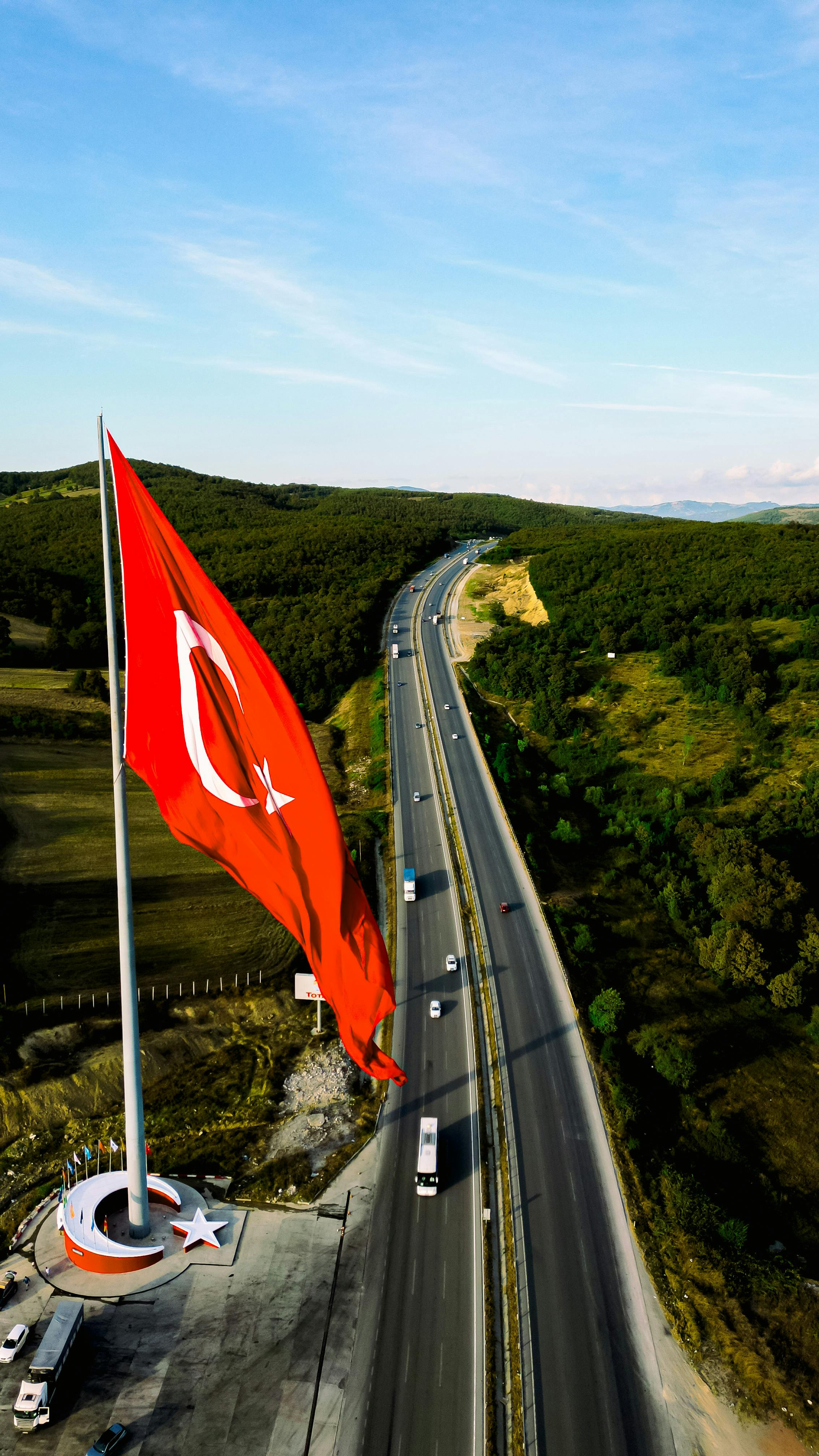 Turkish flag waving over a highway amidst green landscapes.