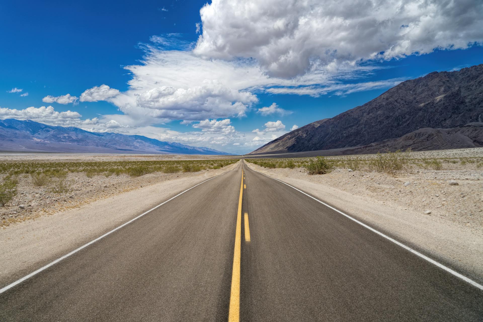 Desolate straight road stretching into a desert landscape under a bright blue sky.