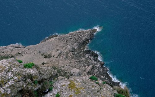 Free Stunning aerial shot of rugged coastline meeting deep blue ocean waters with rocky formations. Stock Photo