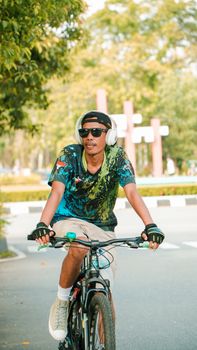 A young man with headphones rides a bicycle on a city street under the sun. - Fotografer Sidoarjo