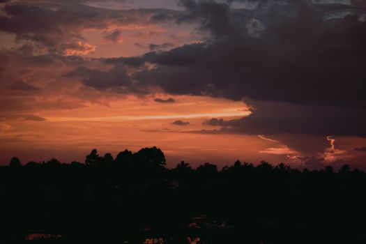 A vivid sunset sky with dark cloud formations and silhouette trees.