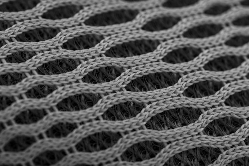 Close-up of a grey nylon knit, open hexagonal cells held by fine synthetic yarn.