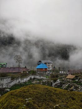 雾气缭绕的山地间，坐落着一个宁静的村庄，屋顶和绿地随处可见