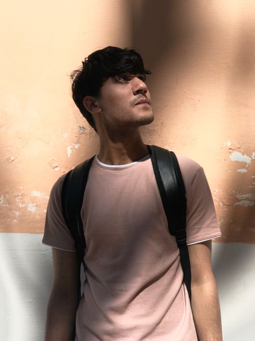 Free Backlit portrait of a young man standing against a textured wall with shadows. Stock Photo