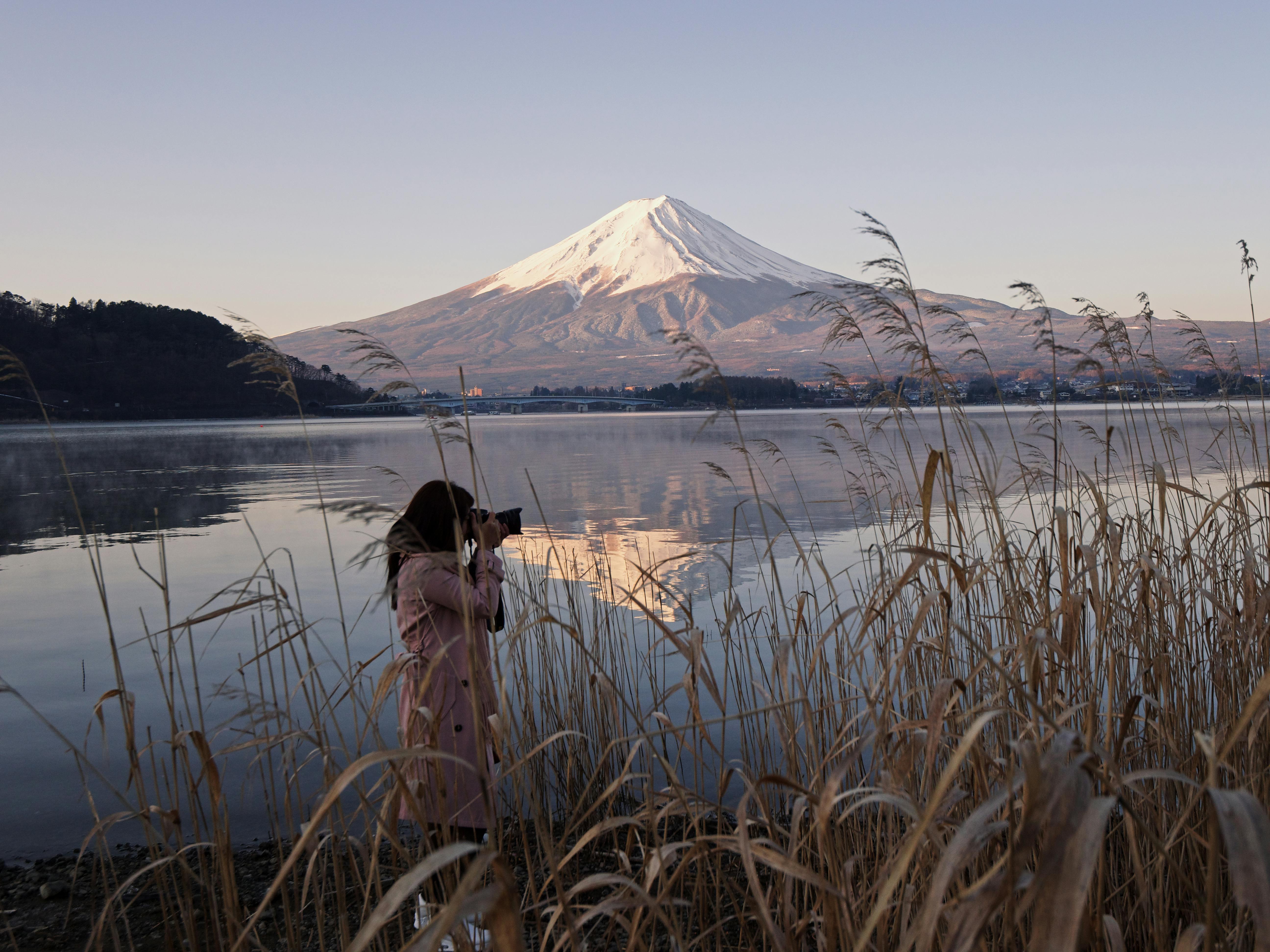 woman taking picture near lake with view of mount fuji