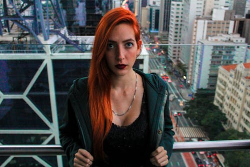 Free Portrait Photo of Woman Standing in Front of Glass Wall With  Cityscape in the Background Stock Photo