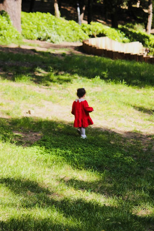 A little girl in a red dress is walking in the grass