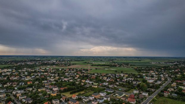 A drone captures a scenic aerial view of a countryside town surrounded by lush fields and under an overcast sky.