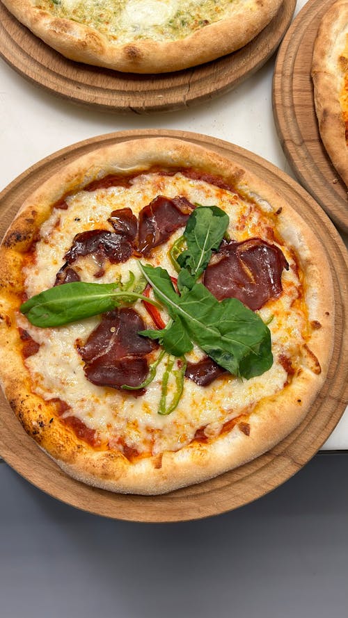 Three pizzas on wooden trays with cheese and spinach