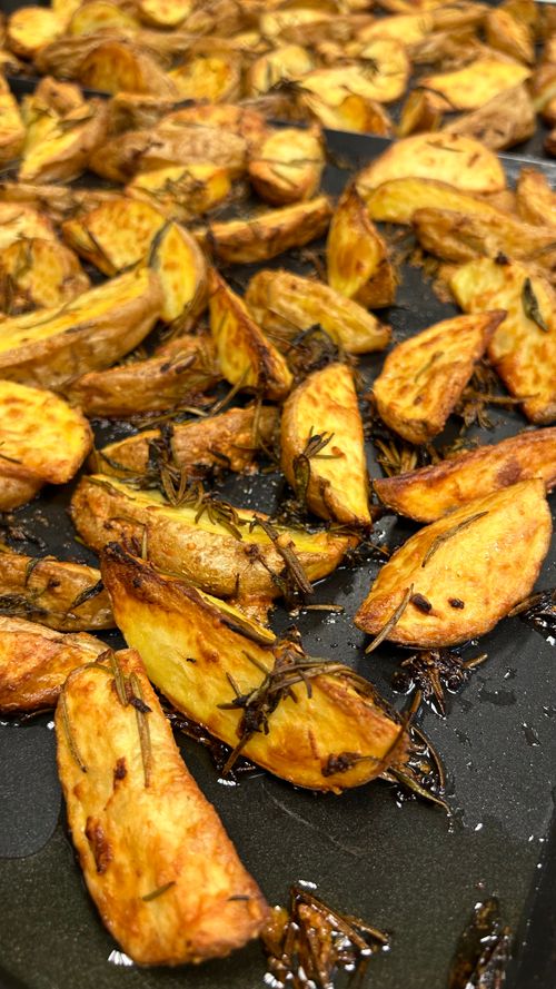 Free Freshly roasted potato wedges seasoned with rosemary, creating a golden crispy texture, perfect for food photography. Stock Photo