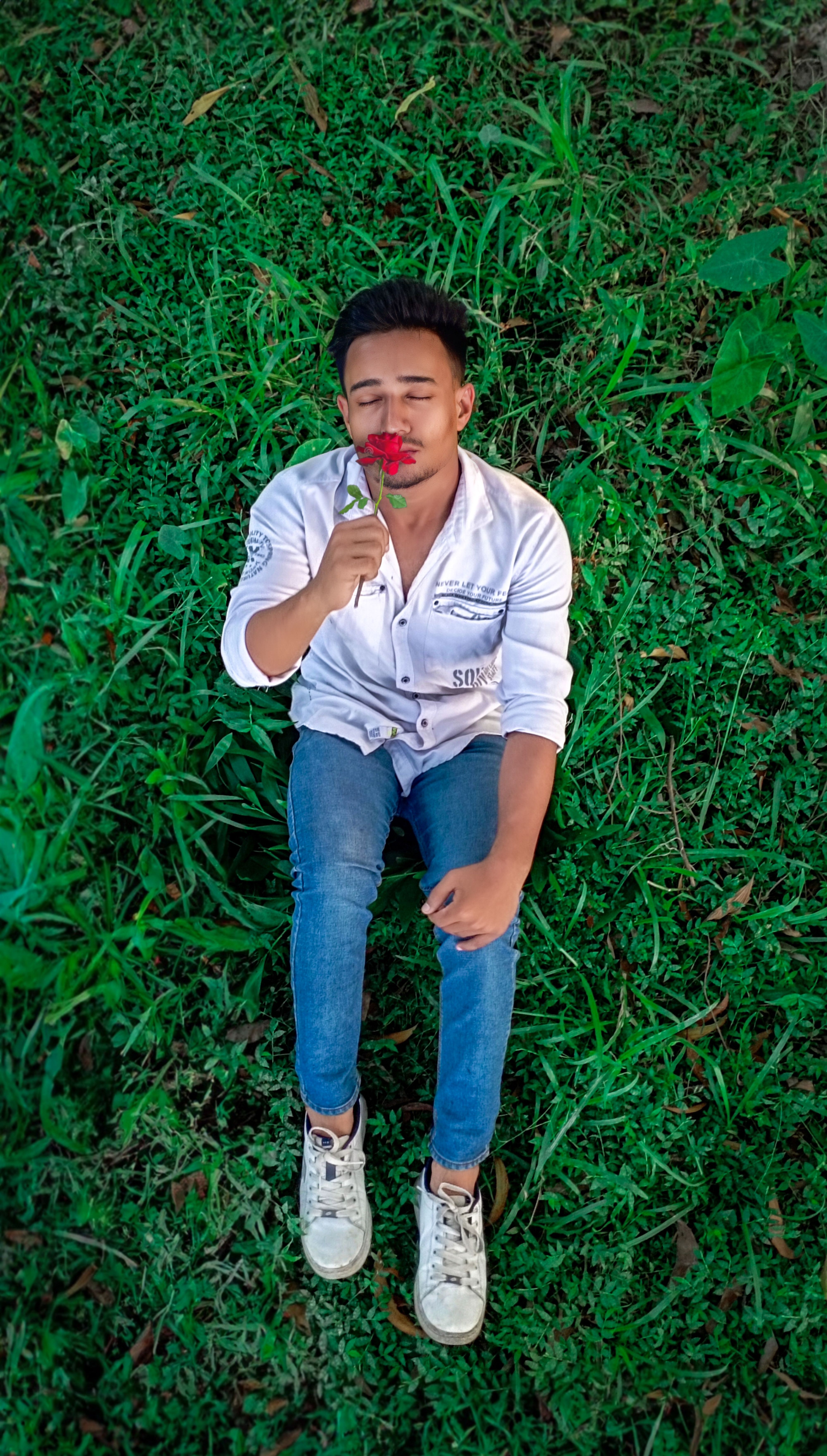 A young man relaxes in a meadow, eyes closed with a red rose, evoking serenity.