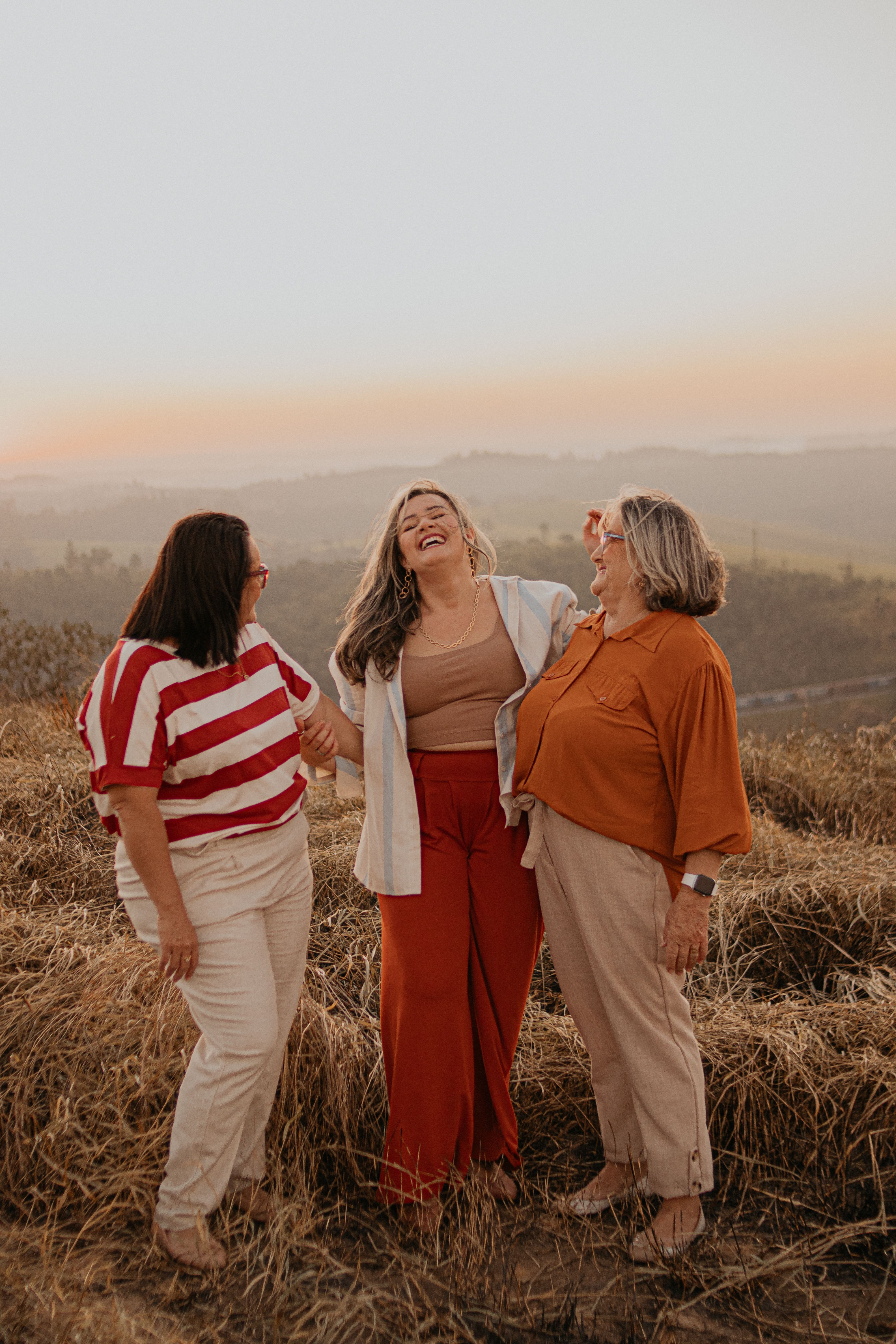 Three women sharing a joyful moment on a meadow, São Paulo, Brazil, during sunset.