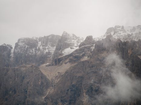 Foggy, atmospheric mountain range in Selva di Val Gardena, Italy, showcasing rugged peaks.