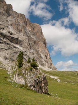 Breathtaking rocky cliffs and lush fields under a clear blue sky in Selva di Val Gardena, Italy.