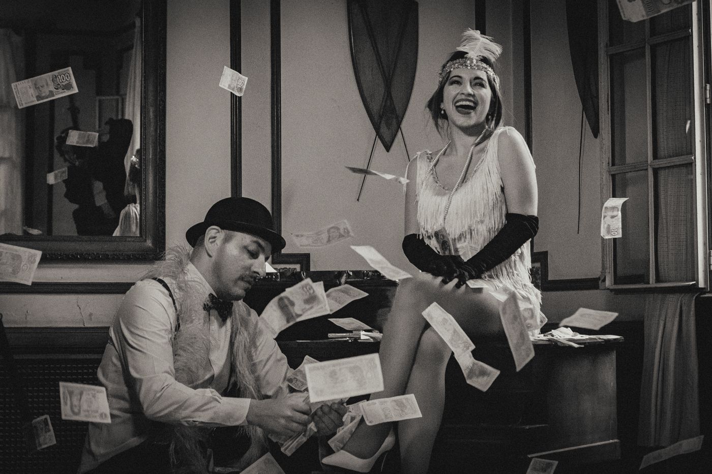 1920s-themed couple in suits and flapper dress with flying money indoors.