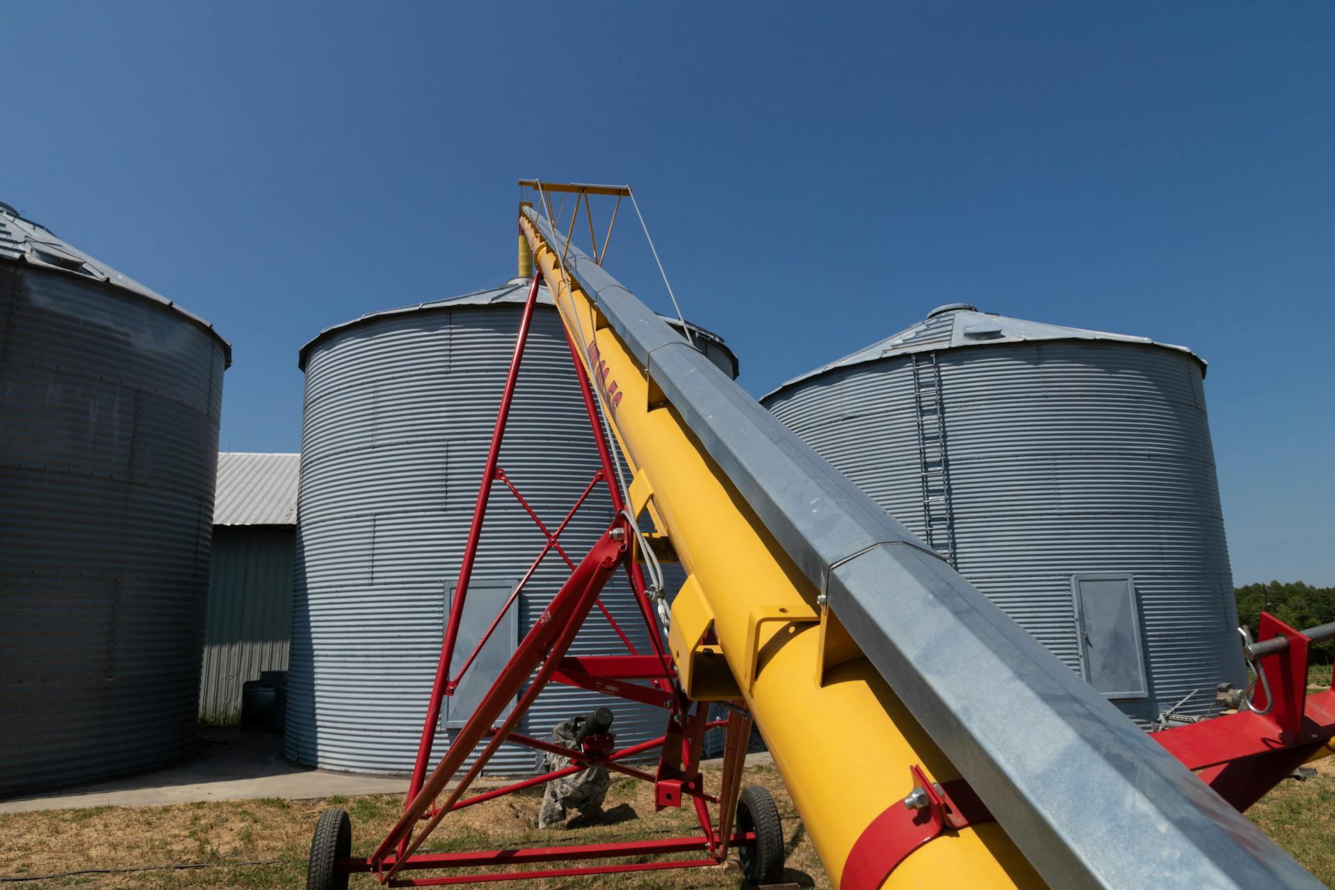 Steel grain silos with a yellow conveyor in a North Carolina farm under a clear blue sky.