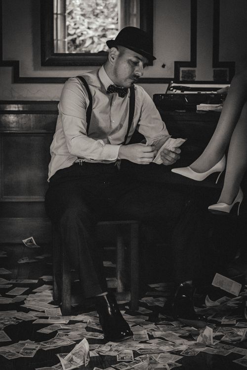 Free Black and white photo of a vintage-themed man counting money indoors, surrounded by scattered bills. Stock Photo