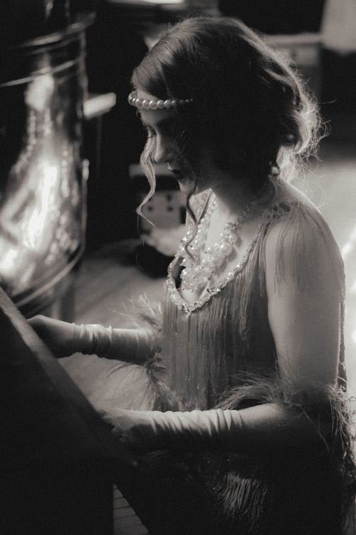 Free Side profile of a woman in 1920s flapper dress seated at a piano, creating a vintage black and white scene. Stock Photo