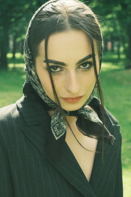 Free Elegant woman in a headscarf and jacket poses in a lush green park, showcasing fashion and beauty. Stock Photo