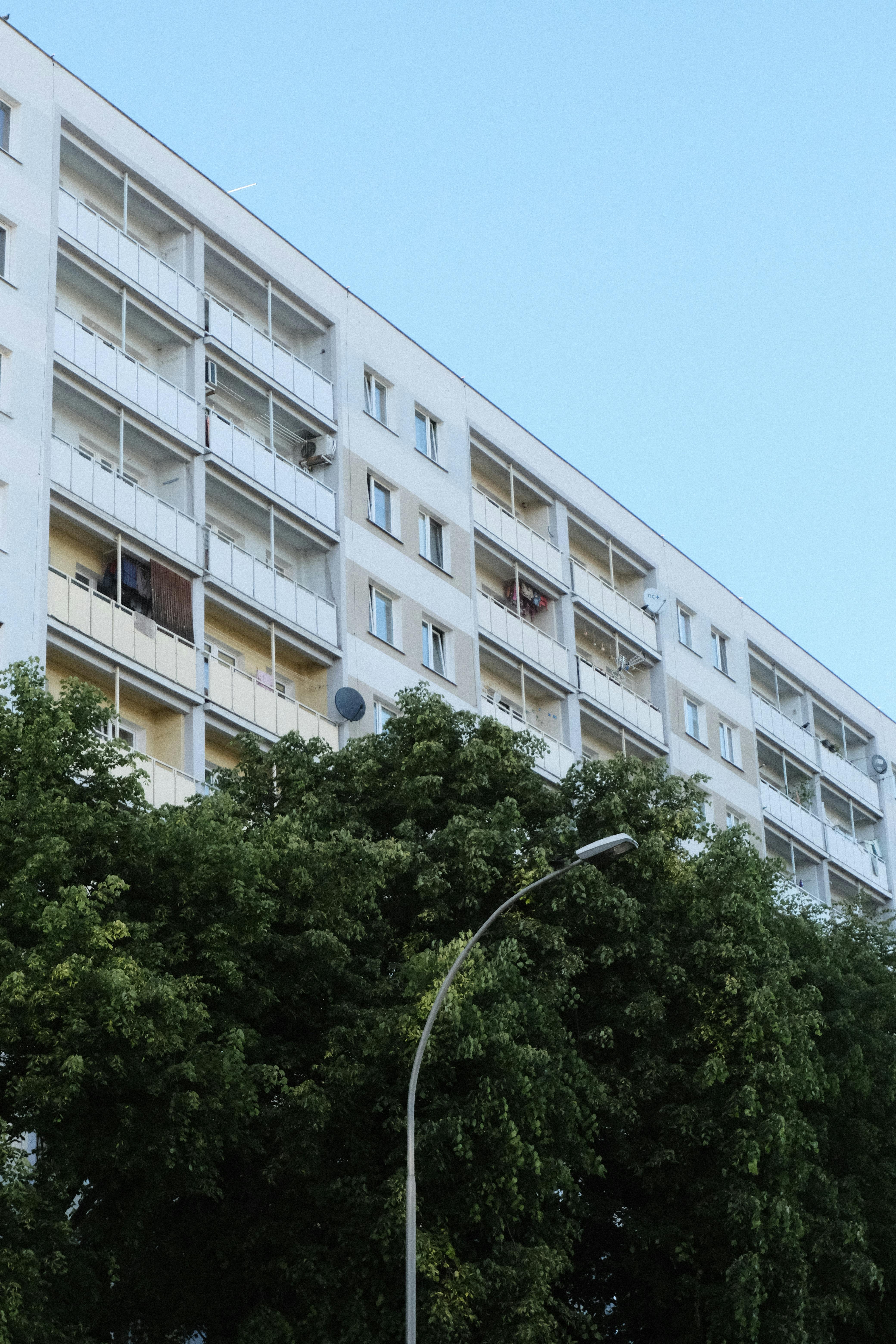 High-rise residential building with balconies and satellite dishes amidst lush urban greenery.