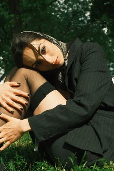 Portrait of an elegant woman in a black suit sitting in a park wearing a headscarf.