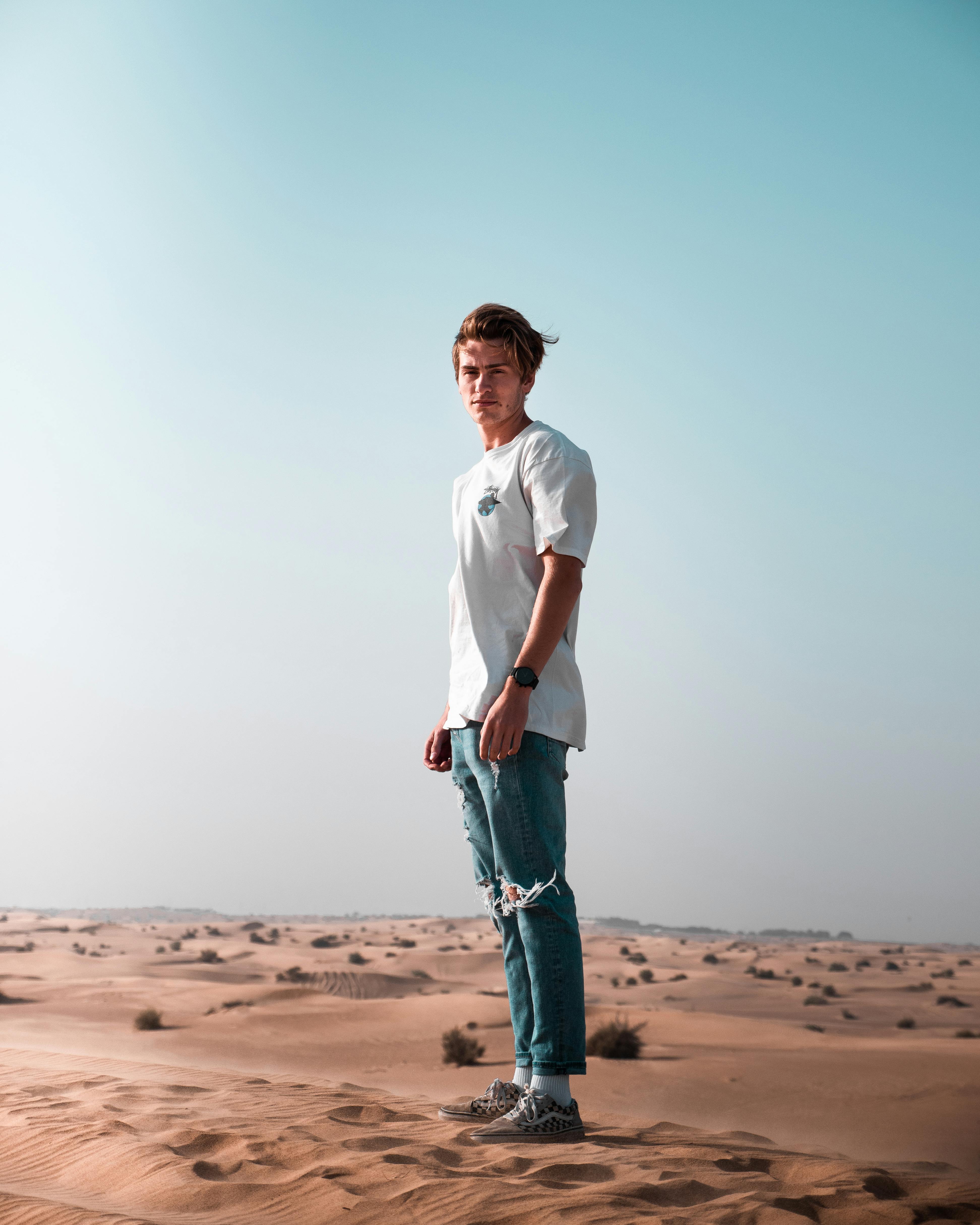 一名年轻人站在迪拜充满活力的沙漠中，头顶是蔚蓝的天空