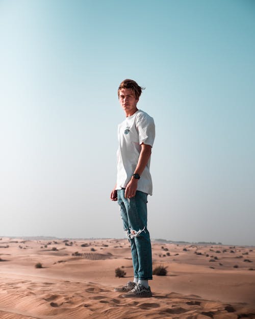 Man wearing a white t-shirt and blue denim pants standing on sand
