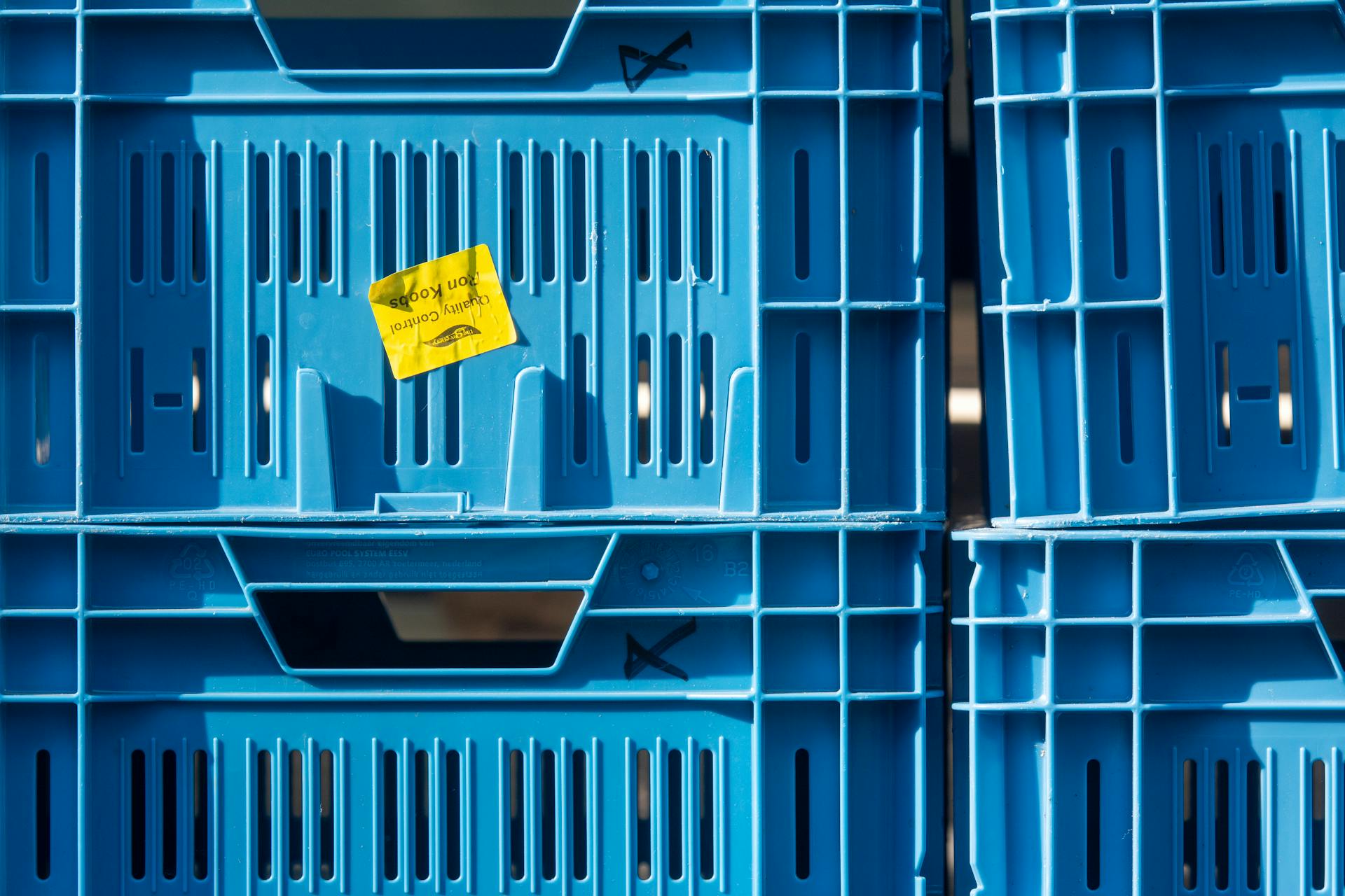 Close-up of stacked blue plastic crates with a quality control label.