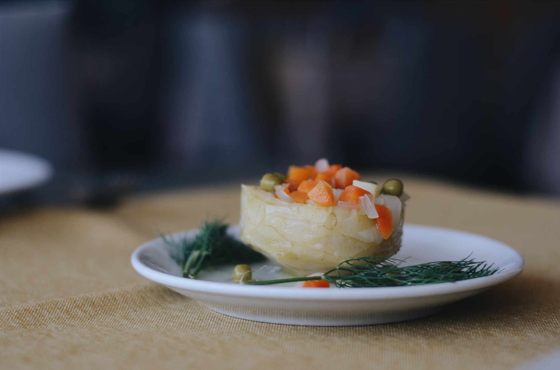 Close-up of a healthy artichoke salad with carrots and peas on a white plate, garnished with herbs.