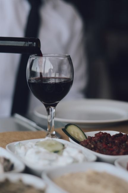 A glass of deep ruby non-alcoholic wine next to a small saucepan of simmering grape juice, cinnamon stick, and star anise on a wooden board.