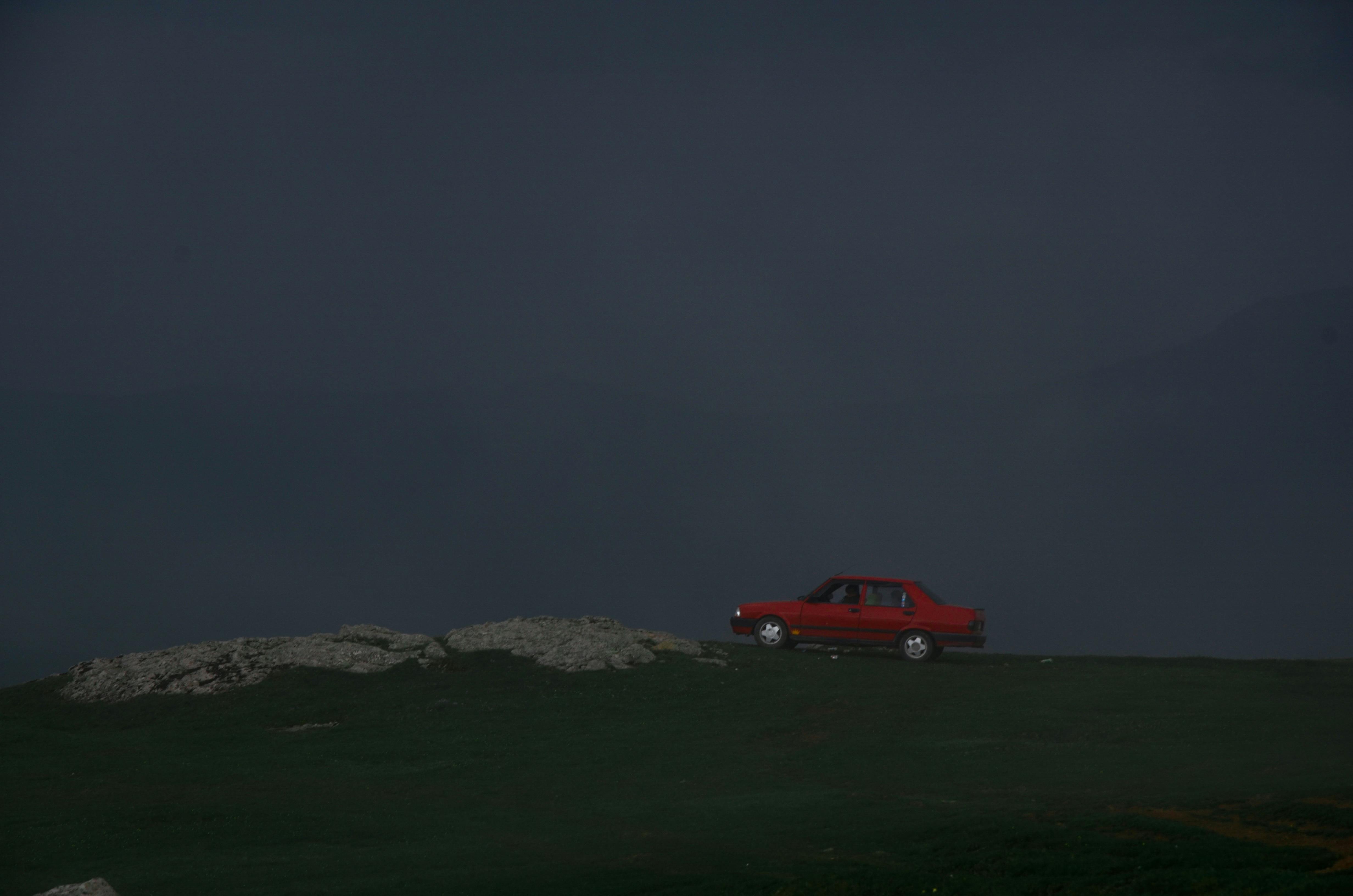 雾蒙蒙的山顶上，一辆红色的汽车孤零零地停在漆黑的天空下