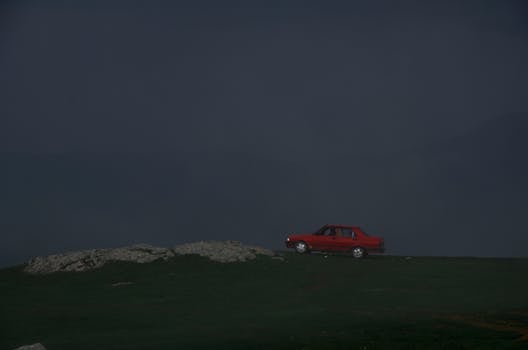 雾蒙蒙的山顶上，一辆红色的汽车孤零零地停在漆黑的天空下