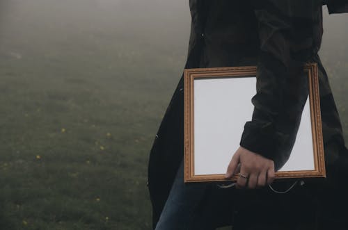 Close Up of Person Wearing Long Jacket  Carrying Brown Framed Mirror 