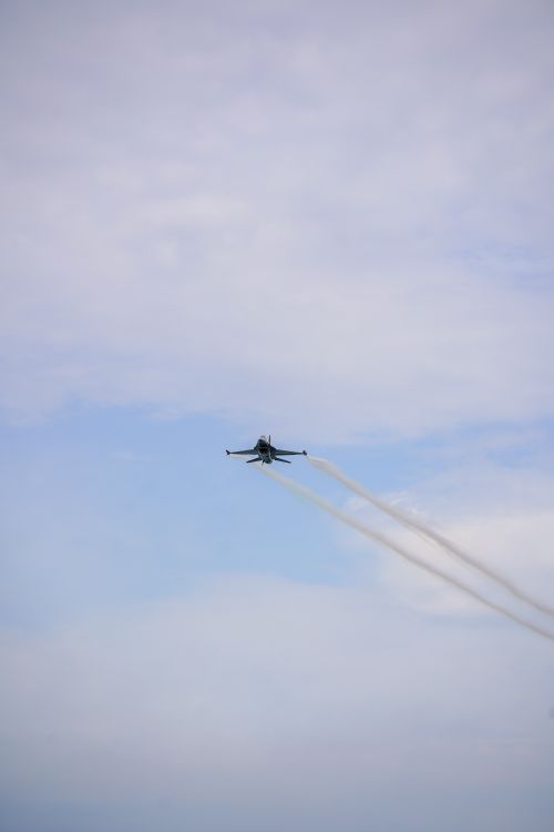 Free Military jet flying high with visible contrails against a clear sky. Stock Photo