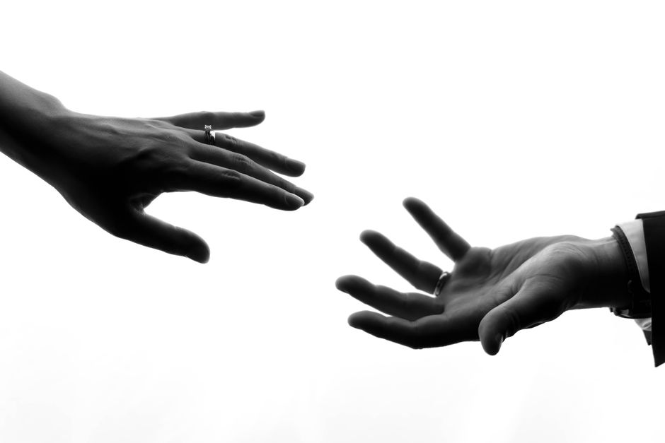 Elegant black and white photo of bride and groom hands with rings reaching towards each other.
