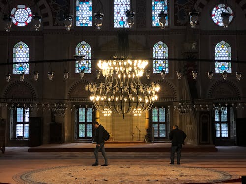 Two men stand in front of a large chandelier