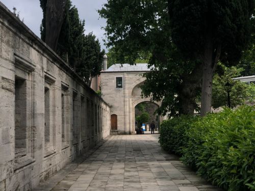 Free A serene pathway lined with stone walls and vibrant greenery, leading to an ancient archway. Stock Photo