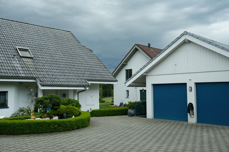 Lovely suburban houses with blue garage doors under cloudy sky, surrounded by greenery.