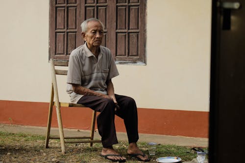 家の外の木製の椅子に座っている老人の写真