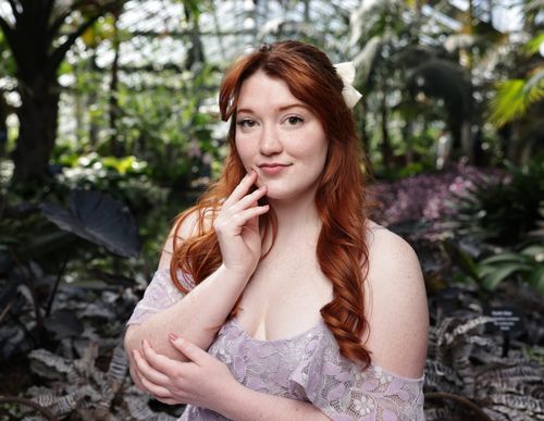 Free A young caucasian woman in an ivory lace dress poses gracefully in a lush greenhouse. Stock Photo